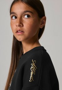 Sudadera negra con cuello redondo, puños acanalados y logo bordado en dorado "AllSaints" en el hombro izquierdo. Textura suave.