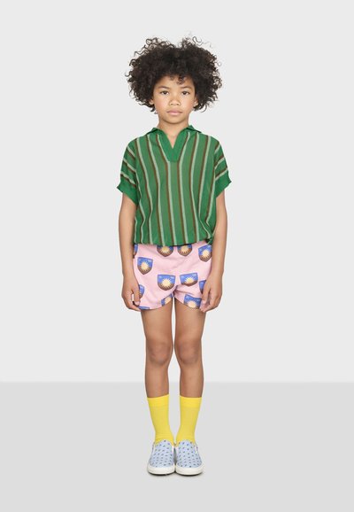 Zeleno pruhovaná krátká košile, růžové šortky s designem slunce, žluté ponožky a modré slip-on boty s tečkovaným vzorem.