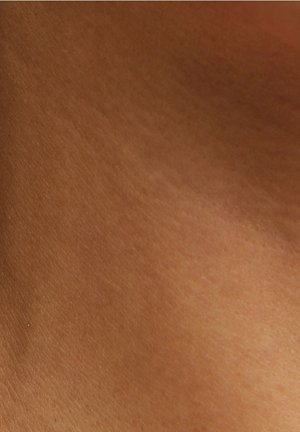 Gros plan sur une peau brune lisse et uniformément teintée, avec une texture naturelle et de subtiles variations de lumière.