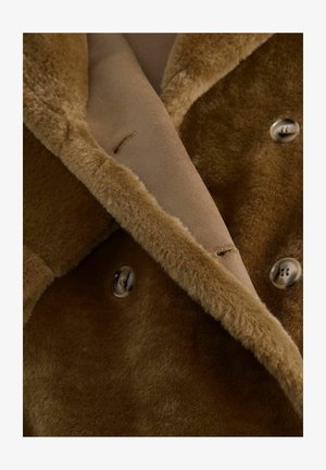 Manteau en shearling brun avec une texture lisse et douce, featuring un design à double boutonnage et de gros boutons, orné d'une doublure intérieure contrastante.