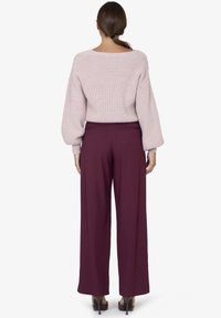 Maglione a maglia di un rosa tenue con maniche ampie abbinato a pantaloni bordeaux a vita alta e dalla vestibilità ampia. Tessuto morbido e design sartoriale.