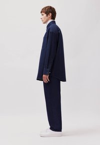 Dunkelblaue Jeanshemd mit einer Brusttasche, lockerer Schnitt und langen Ärmeln, kombiniert mit passenden dunkelblauen Jeans und weißen Turnschuhen.