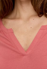 Rosa V-ringad topp med ett strukturerat tyg, med en grund V-formad halsringning och rena sömmar längs kanterna.