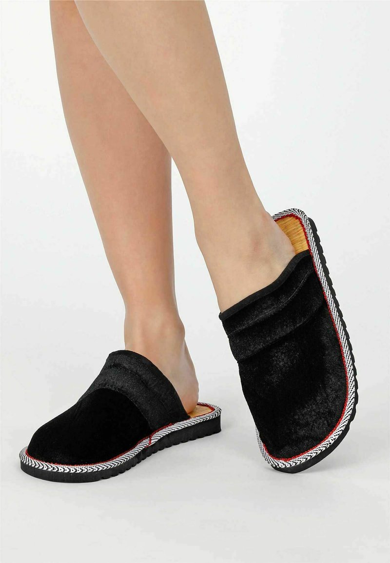 Schwarze Stoff-Clogs mit einer weichen Textur, featuring einem schlupfbaren Design, roten Nähten und einer strukturierten schwarzen Sohle.