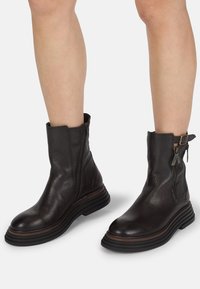 Botas de tobillo de cuero negro con un acabado texturizado, que cuentan con un cierre lateral de cremallera y un diseño de suela en capas y contraste.