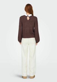 Brun stickad tröja med vida ärmar, nyckelhålsdetalj på ryggen, matchad med högmidjade vita byxor och beigefärgade klackskor.