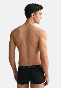 Black boxer briefs with a logo waistband, made of smooth fabric, fitted design, and a low-rise cut, displayed on a bare torso from the rear.
