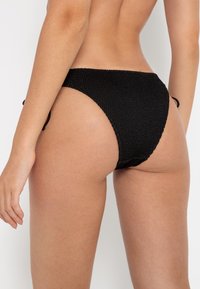 Čierne pletené bikiny s vysokým strihom, so zaväzovacími bokmi a štruktúrovaným materiálom. Hladký okraj po stranách.