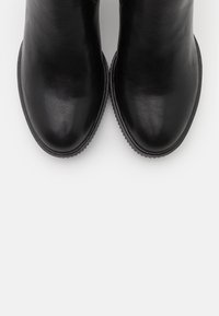 Botas de tobillo de cuero negro con textura suave, punta redonda y suelas de goma. Sin adornos ni patrones visibles.