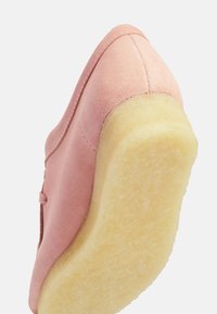 Rosa mockaskor med rund tå och en texturerad gul gummisula, med sömdekoration längs den övre kanten.