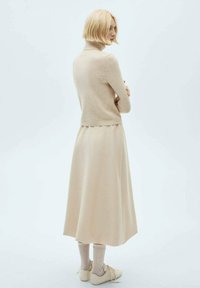 Beige højhalset sweater med blød struktur. Lang, svajende beige nederdel med en scallop-kant, parret med beige sko og ribbede sokker.