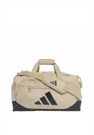 Beige ja musta värinen Adidas matkalaukku olkahihnalla ja etutaskulla, suunniteltu urheiluun tai matkustamiseen.