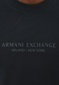 Zwarte katoenen t-shirt met een geribde ronde hals en verhoogde tekst: "ARMANI EXCHANGE MILANO / NEW YORK" in een contrasterende afwerking.