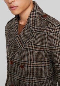 Abrigo de cuadros marrón de doble botonadura con cuello muesca, presenta botones marrones y una tela de mezcla de lana texturizada.