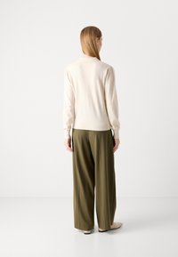 Cremefarvet sweater med pufærmer, struktureret strik, parret med løstsiddende olivengrønne bukser. Fodtøjet er lysfarvet, diskrete flade sko.