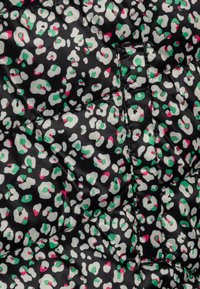 La tela de abrigo acolchada presenta un fondo negro con manchas de leopardo blancas acentuadas en verde y rosa. Textura suave con costuras visibles.