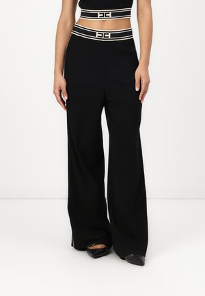 Pantalons larges noirs avec une taille ajustée présentant deux rayures crème et des accents de logo. Tissu lisse avec une silhouette droite.