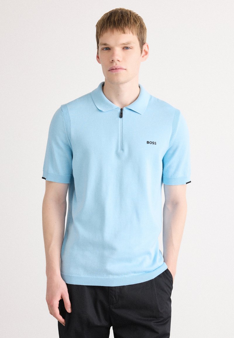 Polo azul claro com mangas curtas, colarinho com fecho éclair e textura canelada. Apresenta um logo preto "BOSS" no lado esquerdo do peito.