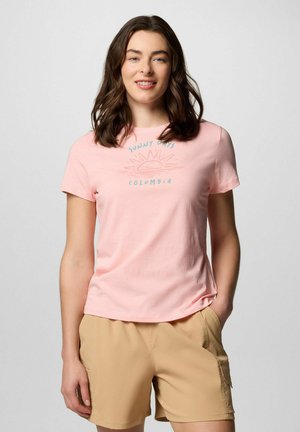 T-shirt en coton rose clair avec un graphique de soleil et le texte "Jours ensoleillés Columbia", associé à un short beige. Manches courtes et col rond.