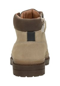 Beige suède enkelboot met een donkerbruine gewatteerde kraag, zwarte trekhaak aan de achterkant en dikke bruine rubberen zool.