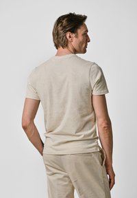 Beige t-shirt met korte mouwen van zacht materiaal, met een eenvoudige ronde halslijn en een casual pasvorm. Achteraanzicht toont de schoudernaden.