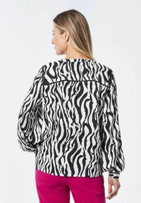 Langmouw blouse met een zwart-wit zebraprint, voorzien van een ronde halslijn en gathered manchetten. Gecombineerd met roze broeken.