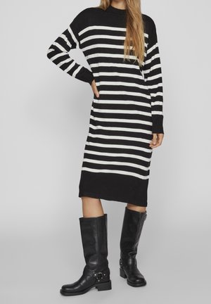 Woman wearing black and white horizontal striped long-sleeve midi dress paired with knee-high black leather boots.
