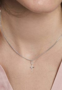 Collar de cadena de plata con un pequeño colgante de cruz, que presenta un acento de gema clara en la parte superior; textura suave contra la piel.