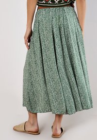 Green pleated midi skirt with white spotted pattern, elastic waistband, and flowy fabric. Worn with beige flat sandals.