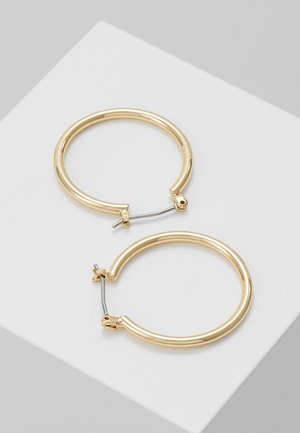 Deux boucles d'oreilles créoles en or poli avec fermoirs à clapet en argent reposant sur une surface blanche avec un fond gris.