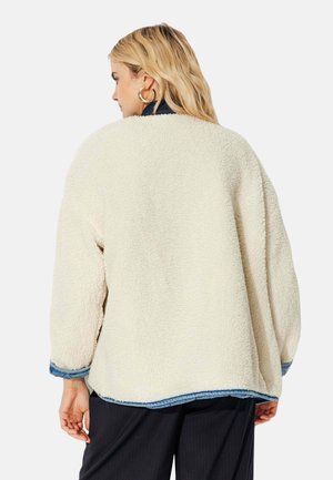 Veste crème floue avec une coupe ample, comportant une finition en denim aux poignets et à l'ourlet, ainsi qu'un tissu à texture douce.