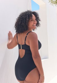 Costume intero nero con schiena scoperta e dettagli in metallo dorato. Tessuto liscio con spalline regolabili per una vestibilità perfetta.