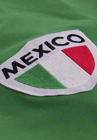 Maillot de sport vert arborant un écusson en forme de bouclier avec le texte "MEXIQUE" au-dessus de trois bandes verticales en vert, blanc et rouge.