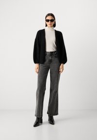 Musta pörröinen neuletakki vaalean turtleneckerin päällä, yhdistettynä korkeavyötäröisiin mustiin farkkuihin ja mustiin teräväkärkisiin nilkkabootseihin. Asusteina aurinkolasit.