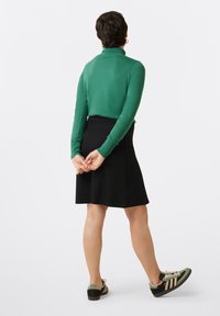 Groen lange mouwen top met een hoge kraag, gecombineerd met een zwarte A-lijn rok en groen-zwart sneakers met beige strepen.