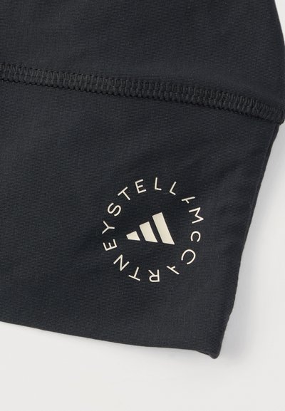 Μαύρο ύφασμα με μανίκι και κυκλικό μπεζ λογότυπο Adidas by Stella McCartney κοντά στη ραφτή ραφή.
