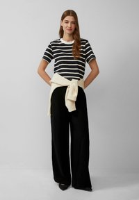 Gestreepte marineblauwe en witte katoenen t-shirt, relaxed fit, gecombineerd met zwarte wijde broek en een crèmekleurige trui om de taille geknoopt.