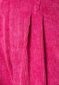 Tela de pana de color rosa intenso que presenta una textura acanalada vertical y un detalle de pliegue, mostrando una apariencia suave y táctil.