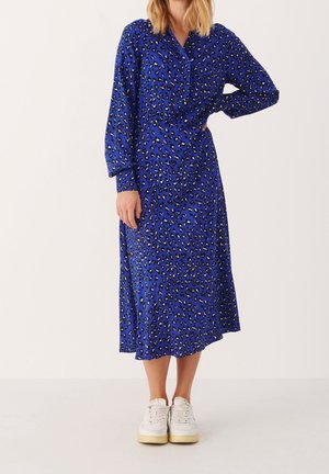 Robe midi à manches longues bleue avec un motif léopard, présentant un devant à boutons et une taille froncée. Associée à des baskets blanches.
