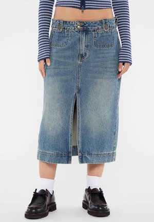 Jupe en denim bleu clair avec une fente à l'avant. Comprend cinq poches, deux boutons à la taille et un ourlet droit.