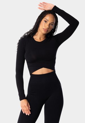 Black long-sleeve cropped top with a round neckline and twisted front, paired with high-waisted black leggings. Smooth texture, fitted design.