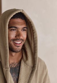 Beez värvusega kapuutsiga riietus, millel on tekstuuriga kangas ja pehme vooder. Omab lõdvestunud istuvust ja püstisi ribasid, kantakse tätoveeritud rinnale.