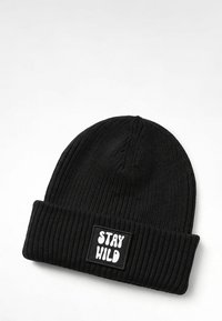 Black knitted beanie with a ribbed texture, featuring a folded cuff and a rectangular patch with the text "STAY WILD" in white.