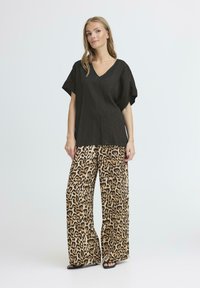 Sort linned V-hals top med korte ærmer, parret med bredbenede leopardmønstrede bukser i beige og brun. Sandaler med lav hæl fuldender looket.