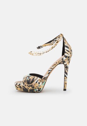 Czarna i złota sandałka na wysokim obcasie z platformą, paskiem wokół kostki z detalem w formie łańcuszka oraz otwartym noskiem.