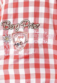 Camisa de cuadros rojos y blancos con el texto bordado "Berg Prinz", un diseño de insignia y acentos florales, con una textura de algodón suave.