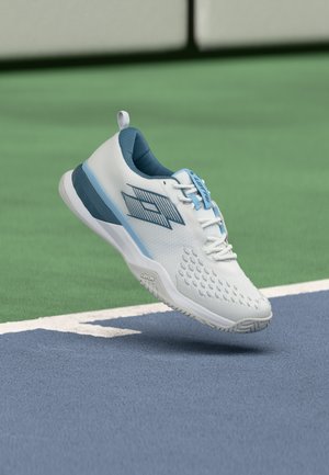 Valkoinen ja sininen urheilukenkä leijuu sinisen ja vihreän tenniskentän pinnan reunalla.