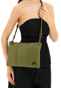 Borsa a tracolla in pelle verde con finitura testurizzata, dotata di cerniera e tracolla regolabile, mostrata su uno sfondo di denim nero.