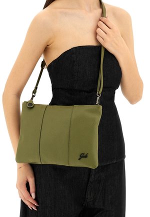 Borsa a tracolla in pelle verde con finitura testurizzata, dotata di cerniera e tracolla regolabile, mostrata su uno sfondo di denim nero.