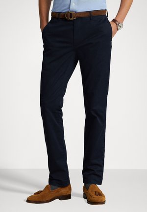 Chinos navy de tela ligera, con un diseño de corte slim, bolsillos laterales y un cinturón de cuero marrón que complementa unos mocasines beige.